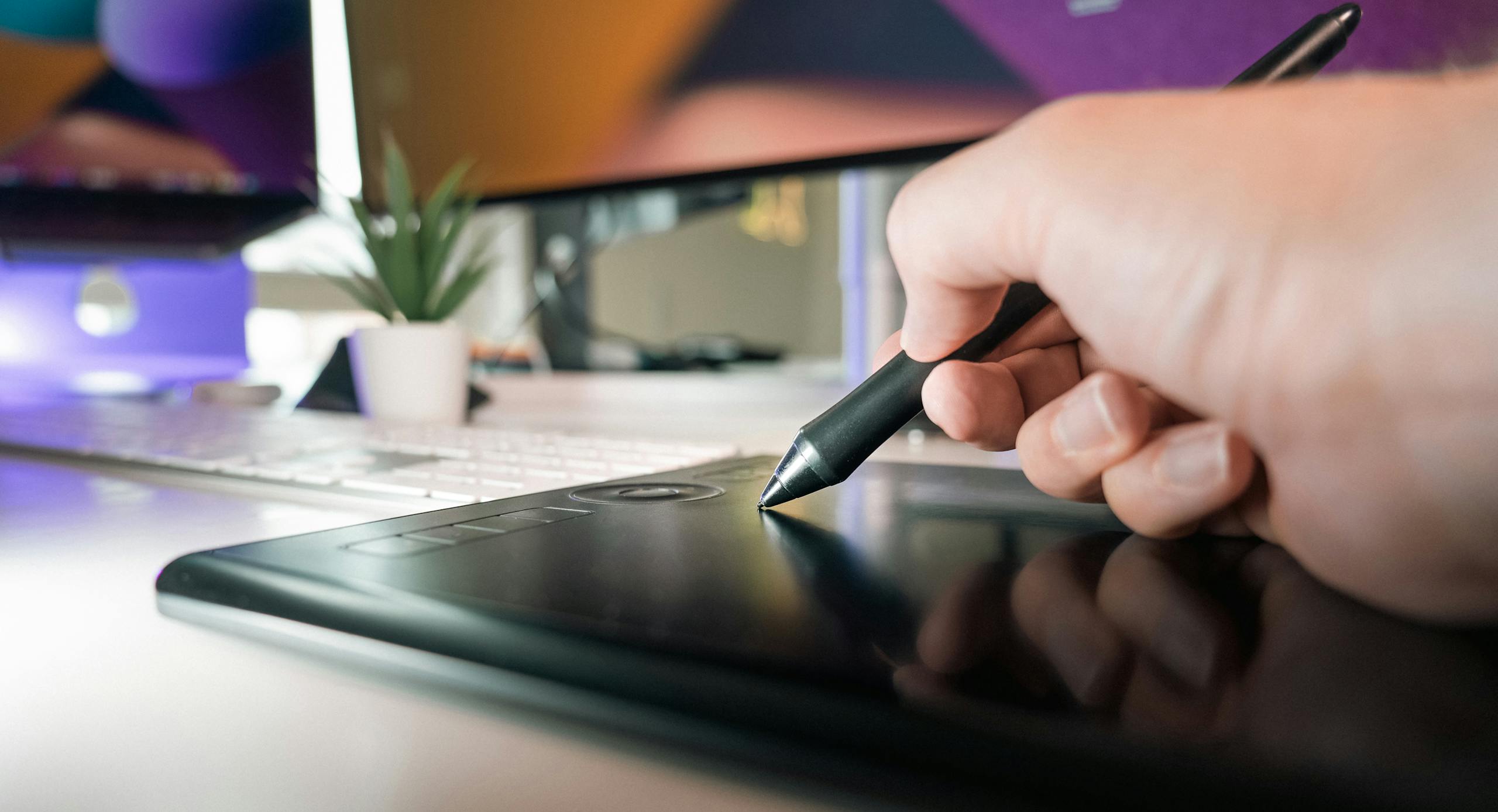 Close-up of a hand using a stylus on a drawing tablet in a modern office setting.